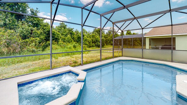 Una piscina con hidromasaje, rodeada por una zona cubierta con estructura de metal y paneles de vidrio.
