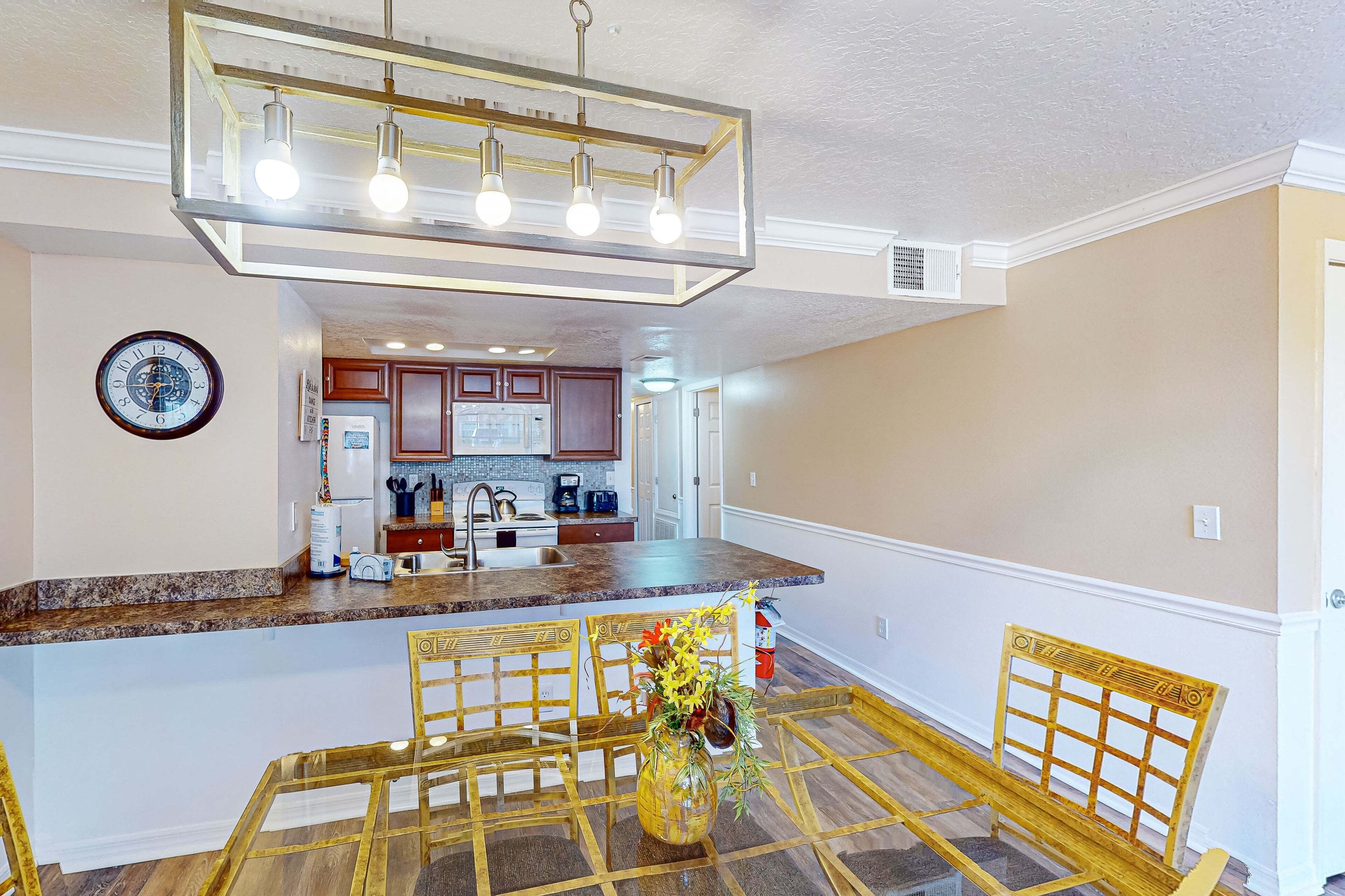 A kitchen with a central island, a dining area with a glass table and chairs, and a hanging light fixture.