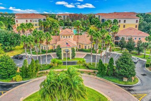 A multi-story hotel with a central courtyard surrounded by palm trees and a parking area. - 3BR/2BA Orlando Condo near Disney with Pool (Orlando)