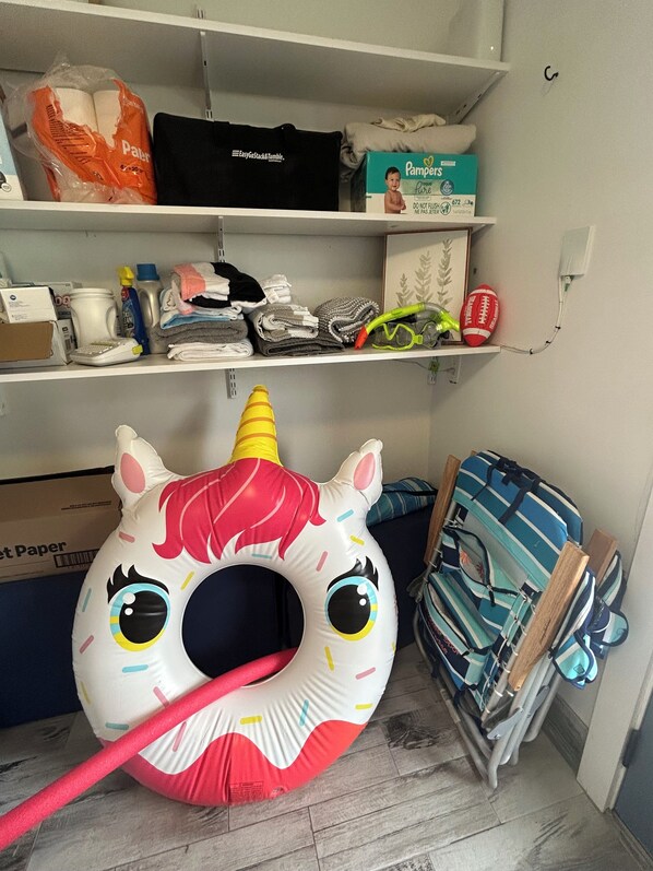 A storage area with shelves containing baby products, a unicorn inflatable, and a blue striped bag.