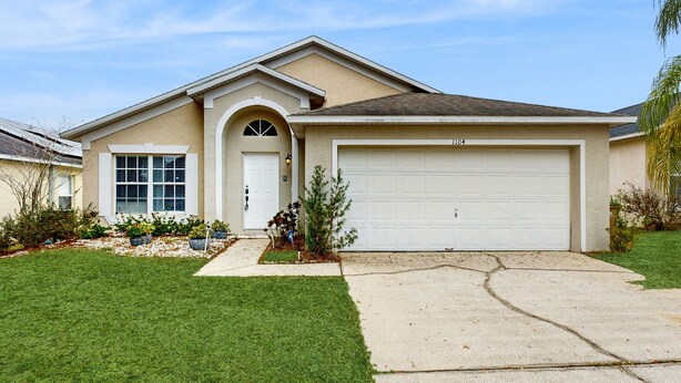 A single-story house with a garage, a front door, and a small front yard with a lawn and some plants. - Single-level home with private pool, close to shopping & attractions (Clermont)