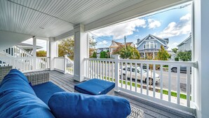 En inglasad veranda med blå kuddar, ett vitt räcke och utsikt över hus och bilar i bakgrunden.