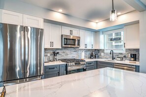 A modern kitchen with stainless steel appliances, a marble countertop, and a tiled backsplash. - Spacious 6BR/4BA Coastal Combo - Ideal for 20 Pax! (Ocean City)