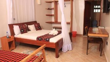 A neatly arranged bedroom with a wooden bed, a bedside table, a chair, a small desk, and a shelf unit.