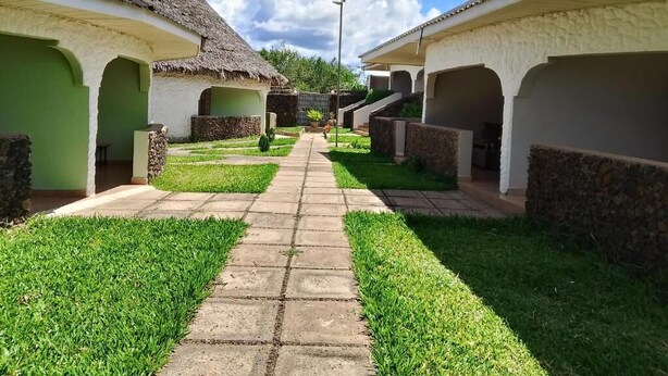 Un sendero conduce a una hilera de cabañas con techo de paja, paredes de piedra y puertas verdes.