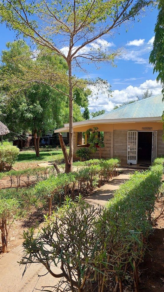 A building with a corrugated metal roof, surrounded by well-maintained greenery and a clear sky.