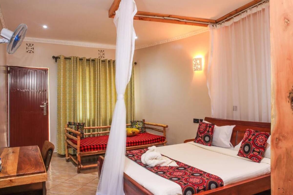 A room with a bed, a wooden chair, a table, and a fan.