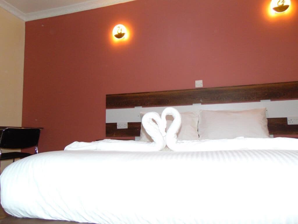 Quarto de hotel com uma cama, duas luzes fixadas na parede e uma cabeceira de madeira.