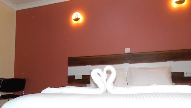 Quarto de hotel com uma cama, duas luzes fixadas na parede e uma cabeceira de madeira.