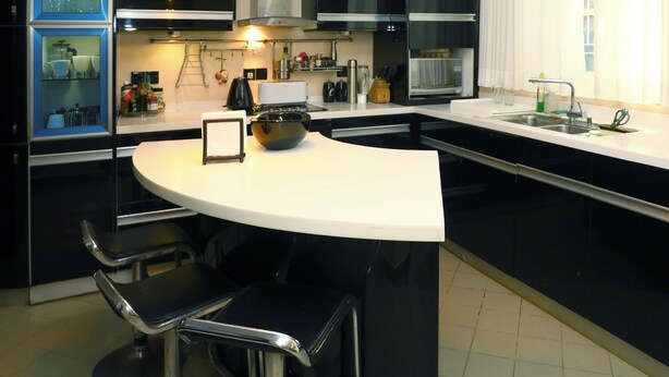 Une cuisine moderne dotée d’un îlot central aux lignes courbes, de tabourets de bar et d’appareils électroménagers intégrés.