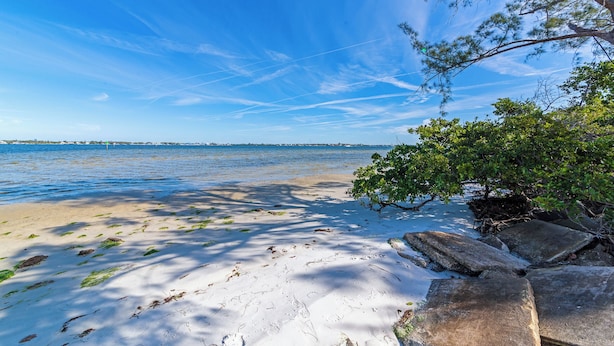Une plage avec un ciel dégagé, une eau calme et des affleurements rocheux.
