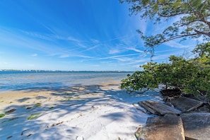 Une plage avec un ciel dégagé, une eau calme et des affleurements rocheux.