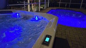 Deux bains à remous dotés d’un éclairage bleu, entourés d’une terrasse couverte agrémentée de guirlandes lumineuses.