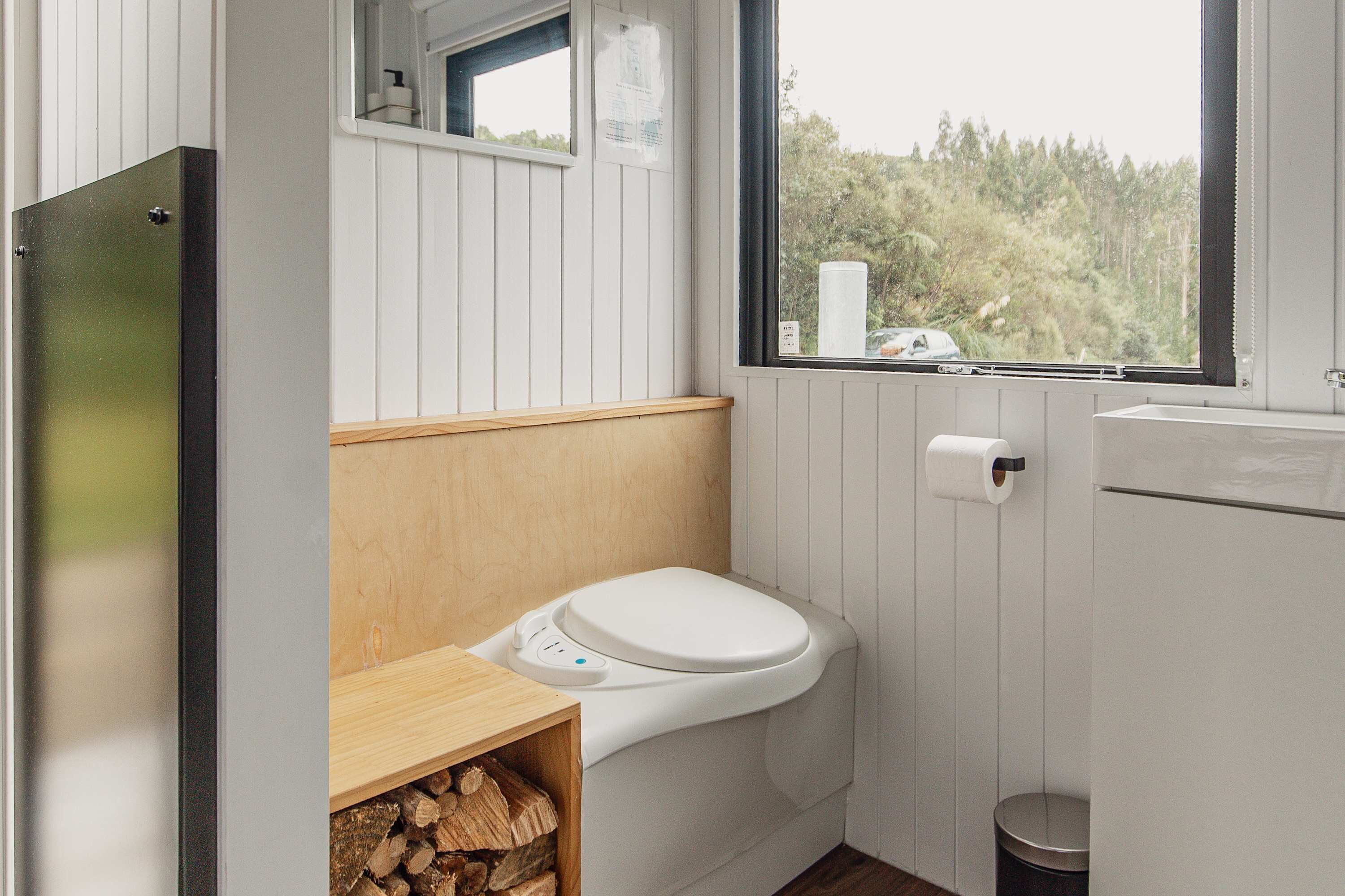 Baño pequeño y funcional con inodoro, una ventana y un dispensador de papel higiénico a la vista.