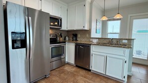 A modern kitchen with stainless steel appliances, white cabinetry, and a granite countertop. - GS6 Shared Heated Pool, Walk to the Beach, Golf Cart Access (Port Aransas)