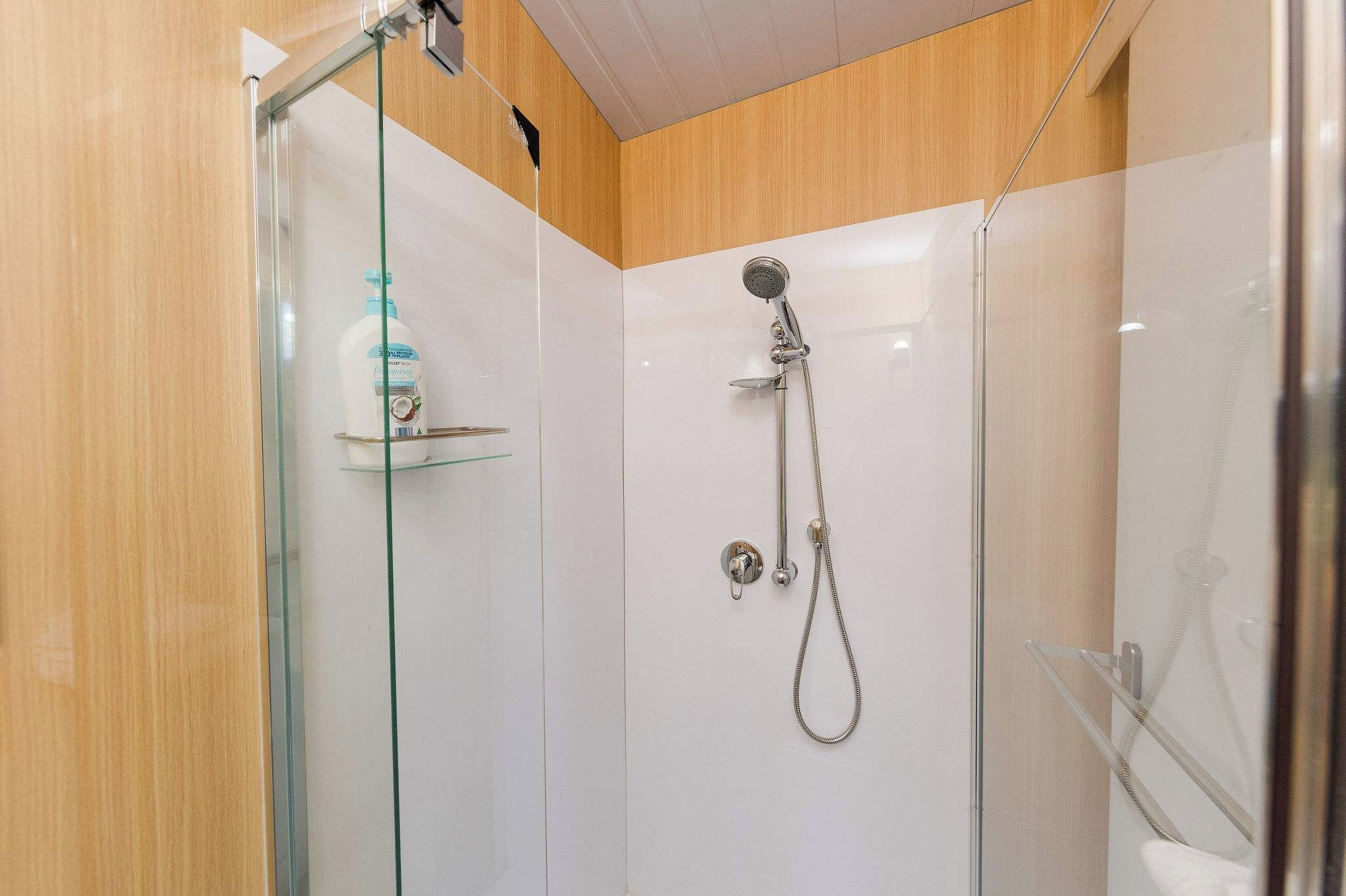 A glass-enclosed shower with a handheld showerhead and a handheld shower attachment.