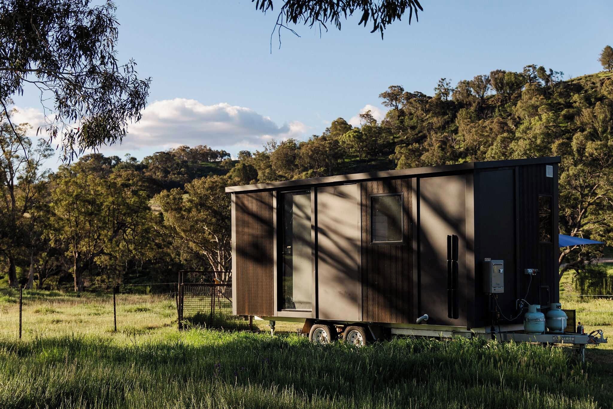 A stationary trailer-style accommodation with a flat roof, a door, and a window, situated in a grassy field with trees in the background.