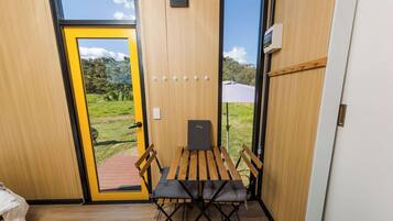 Quarto com porta de madeira, uma pequena mesa, duas cadeiras e um banco.