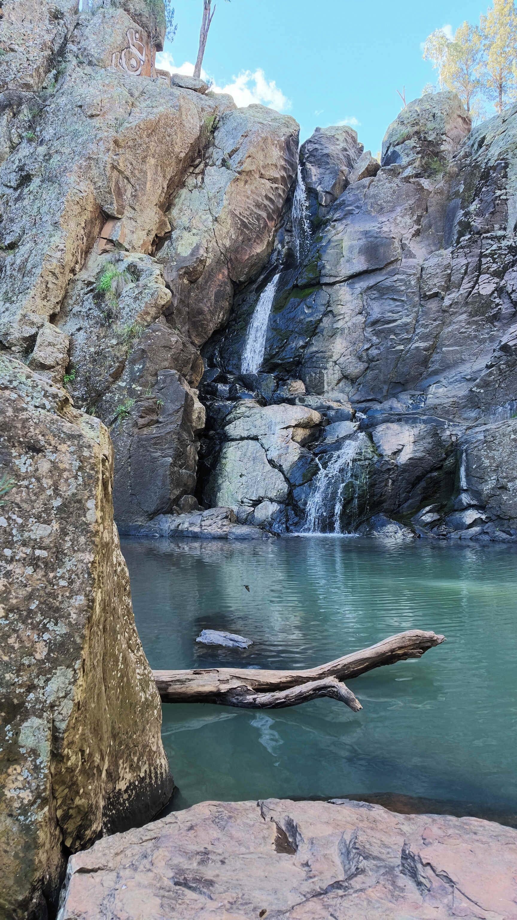 Formación rocosa natural con cascada y una poza de agua cristalina.