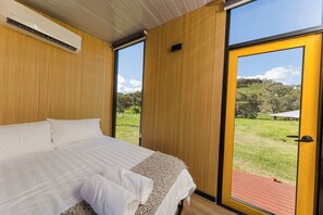 A bedroom with a large bed, wooden walls, and a door leading to a grassy outdoor area. - Waterfall Valley by Tiny Away (Gowang)