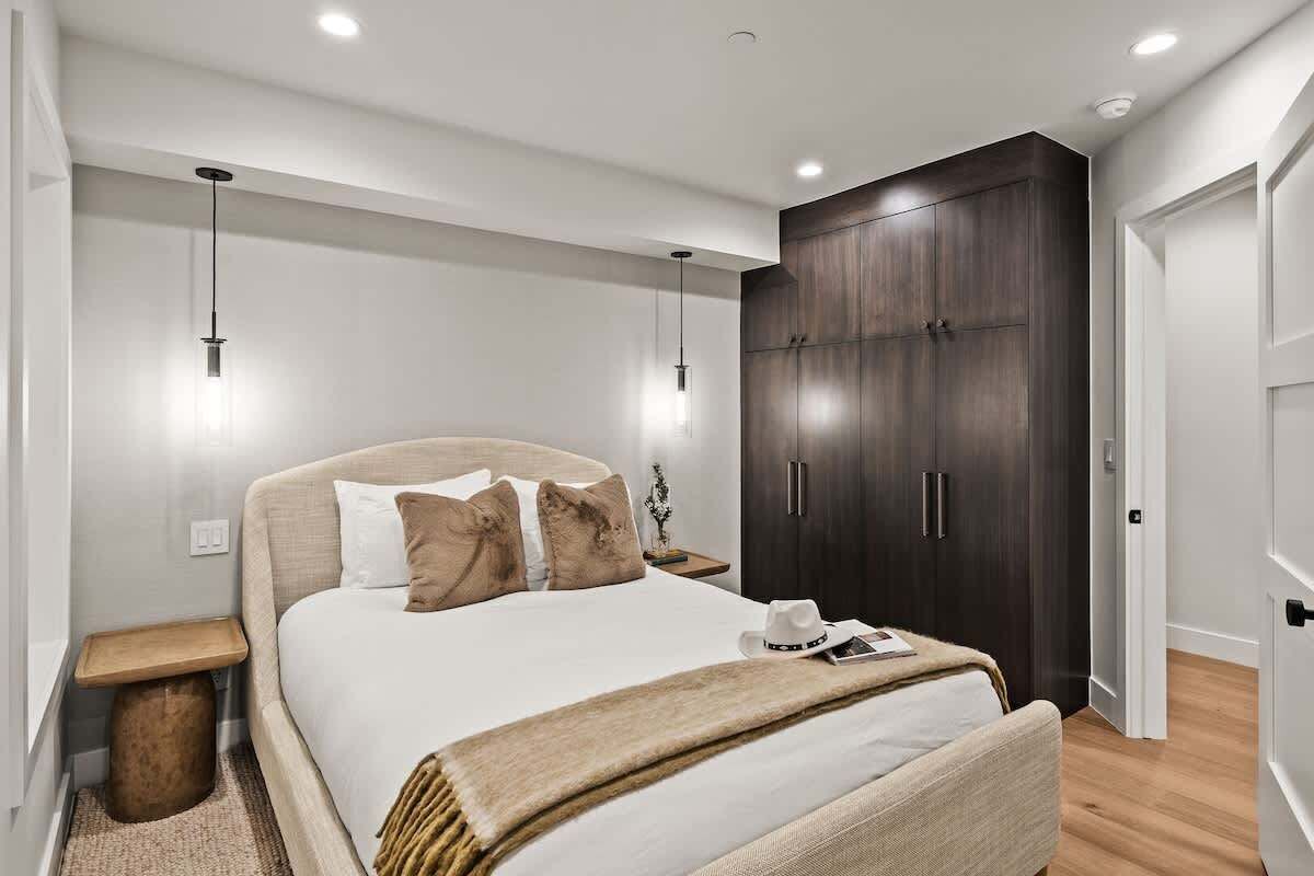 A modern bedroom with a large bed, bedside tables, a wardrobe, and pendant lighting.
