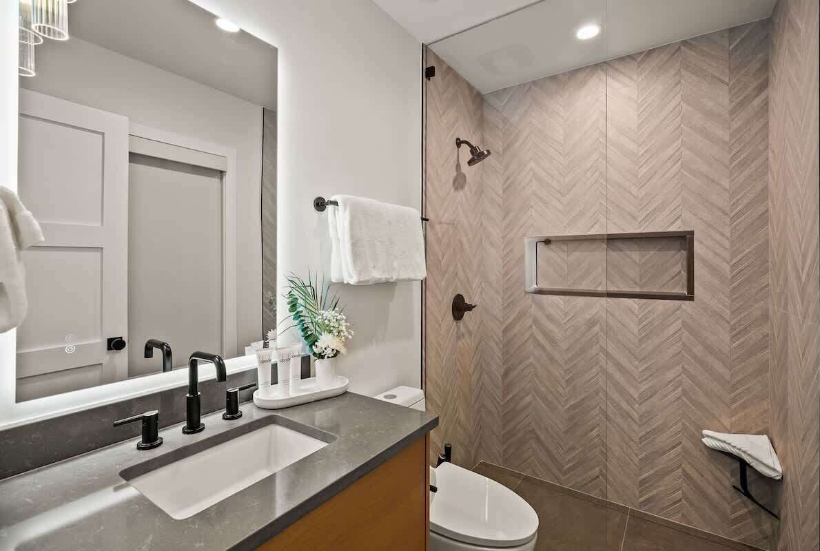 Un baño moderno con un espejo grande, dos lavamanos, una ducha y un inodoro.