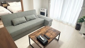 A modern living room with a grey sofa, a wooden coffee table, and a bed in the background. - TOWN ROYAL 601 (Sapporo)