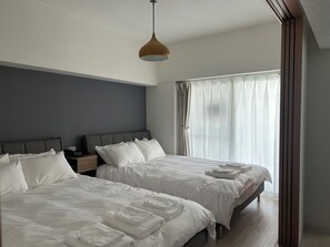 A hotel room with two beds, a wooden headboard, a bedside table, a nightstand, and a large window with sheer curtains. - TOWN ROYAL 601 (Sapporo)