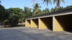 Une rangée de parkings jaunes, avec un sol en béton, entourée de palmiers et sous un ciel dégagé.