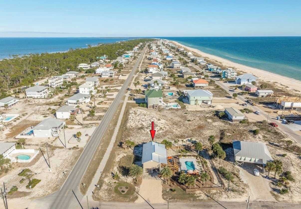 An aerial view of a coastal residential area with houses, a road, and a beach.