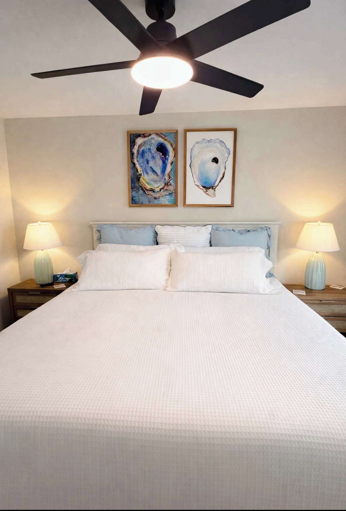 Una cama con ropa de cama blanca, dos cuadros colgados en la pared y dos lámparas de noche.