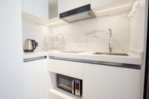 Eine moderne Küche mit weißen Schränken, einer Marmor-Spritzschutzwand, einem Edelstahl-Wasserkocher, einem Wasserkocher-Halter, einer Mikrowelle und einem Spülbecken mit Armatur.
