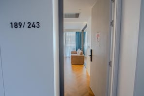 A hallway with a door labeled "189/243" leading to a room with a sofa and a window with blue curtains.