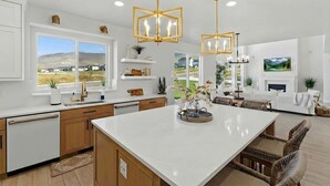 A modern kitchen with white cabinetry, a large island, and pendant lighting. There are windows offering a view of the outdoors. - Modern 6br Deer Valley Retreat | Ski, Golf & Fish (Heber City)