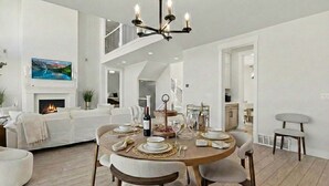 A spacious living room with a fireplace, a dining area set for a meal, and a staircase leading to an upper level. - Modern 6br Deer Valley Retreat | Ski, Golf & Fish (Heber City)