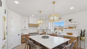 A modern kitchen with white cabinetry, a central island with bar stools, and pendant lighting. - Modern 6br Deer Valley Retreat | Ski, Golf & Fish (Heber City)