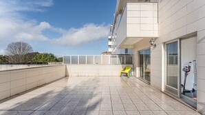 A rooftop terrace with a tiled floor, a yellow and blue chair, and a large window. - GuestReady - Charming Porto retreat with terrace (Boavista)