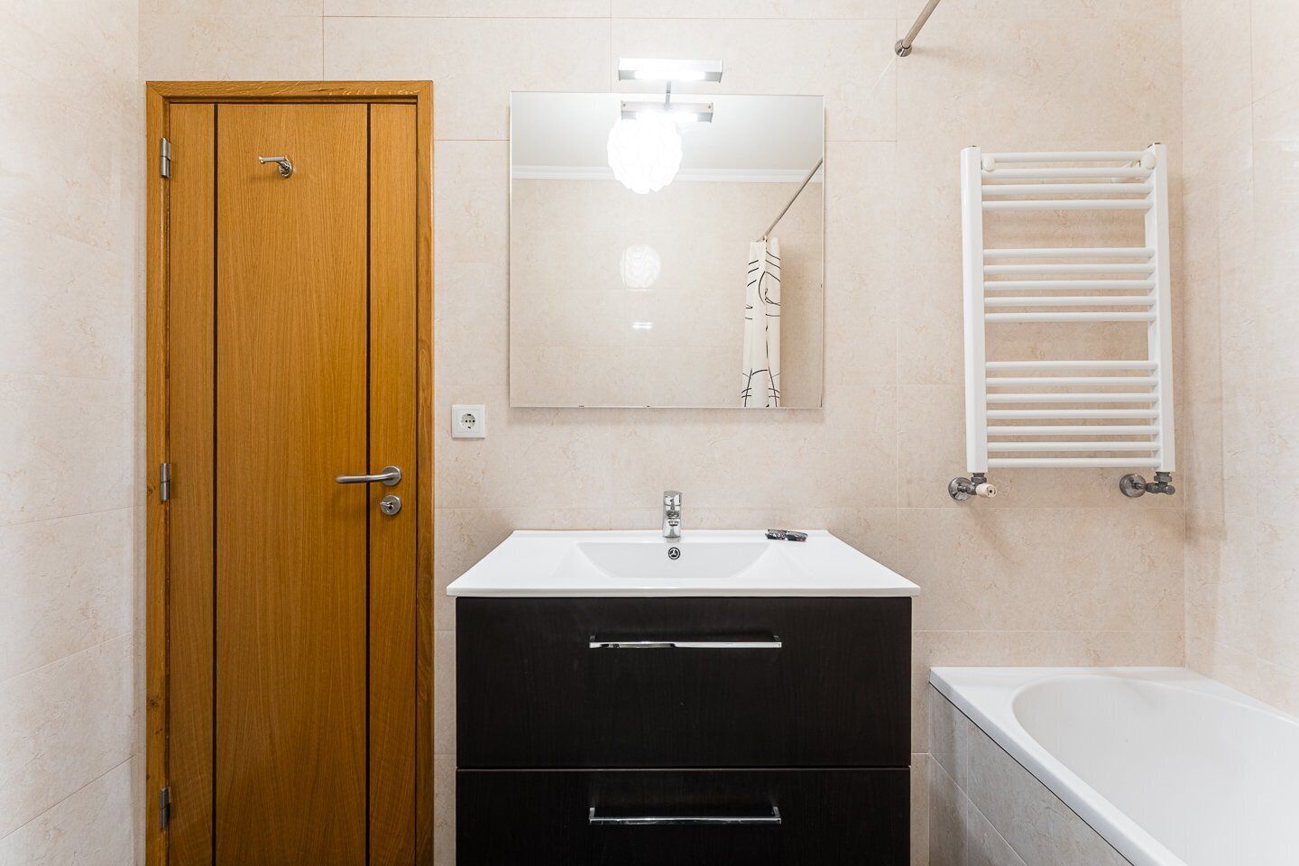 A bathroom with a wooden door, a white sink with a mirror above it, a towel rack, and a bathtub.