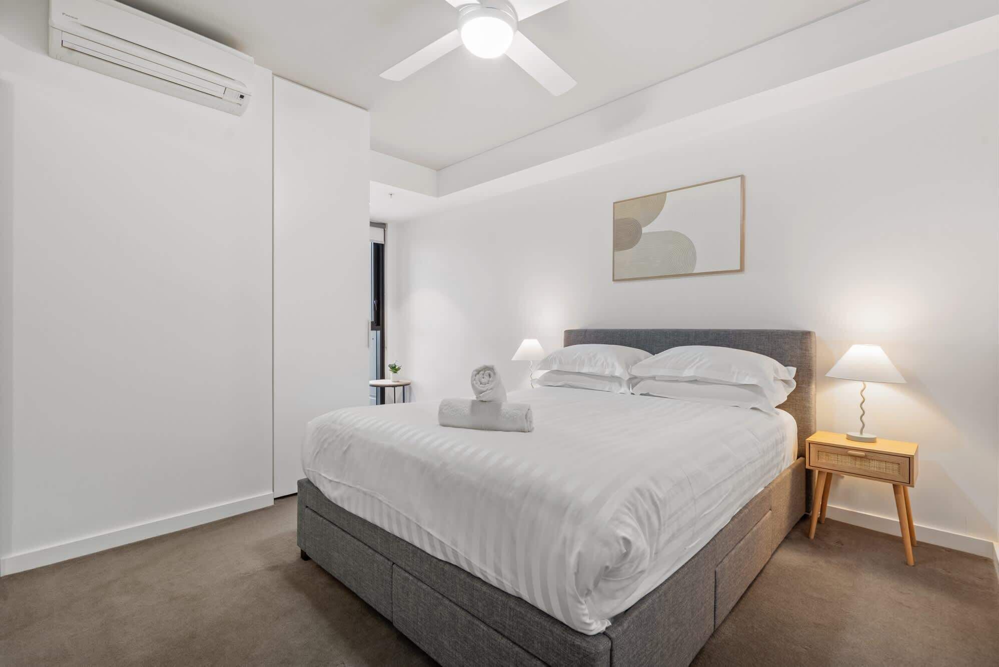 A bedroom with a bed, bedside lamps, a ceiling fan, and a wall-mounted air conditioner.
