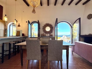 A dining area with a view of the ocean, featuring a table with chairs, a hanging light fixture, and a large mirror on the wall. - " Villa Paola with swimmingpool " (Domus de Maria)