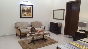 A bedroom with two armchairs, a small table, a dresser, a mirror, and a bed. - 3-bedroom house in enchanting Lahore with cool AC comfort (Lahore)