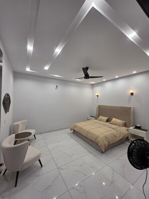 A modern bedroom with a bed, a ceiling fan, a nightstand, and a chair. - Awesome 3-bedroom bungalow on first floor in vibrant Lahore near raya and PKLI (Lahore)