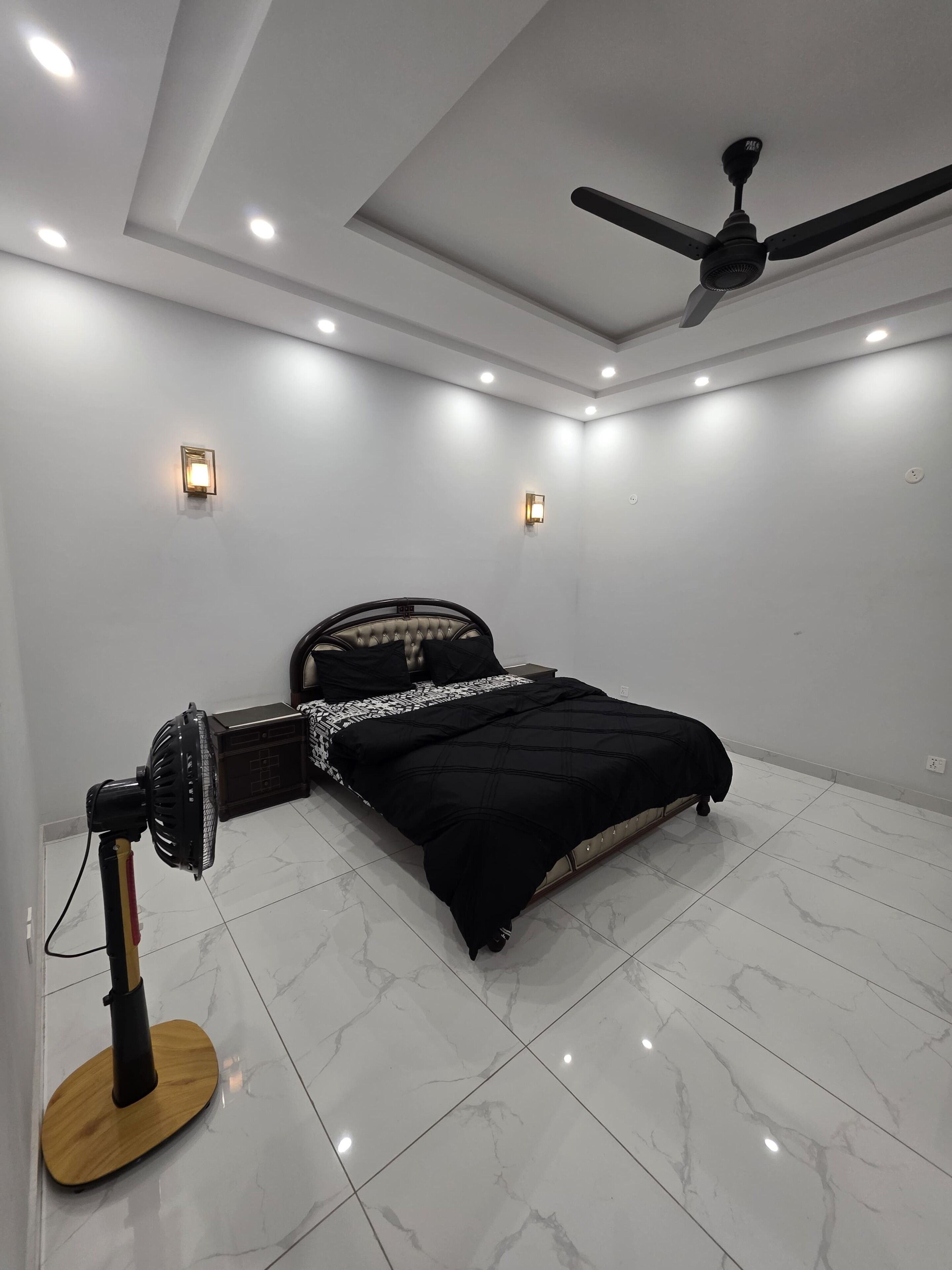Une chambre à coucher comprenant un lit, un ventilateur sur pied, des spots encastrés au plafond et un ventilateur de plafond.