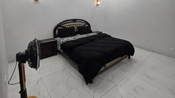Une chambre à coucher comprenant un lit, un ventilateur sur pied, des spots encastrés au plafond et un ventilateur de plafond.