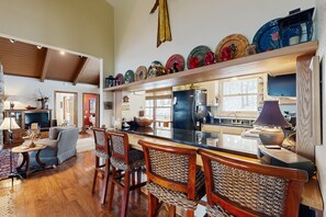 A spacious living area with a wooden floor, a bar with wicker chairs, a television, and a kitchen with a refrigerator and stove. - Adventure Awaits! Beech Mountain Home Near Skiing, Hiking & Trails (Beech Mountain)