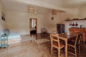 A spacious living area with a dining table, chairs, a sofa, and a kitchen area with a refrigerator and utensils.