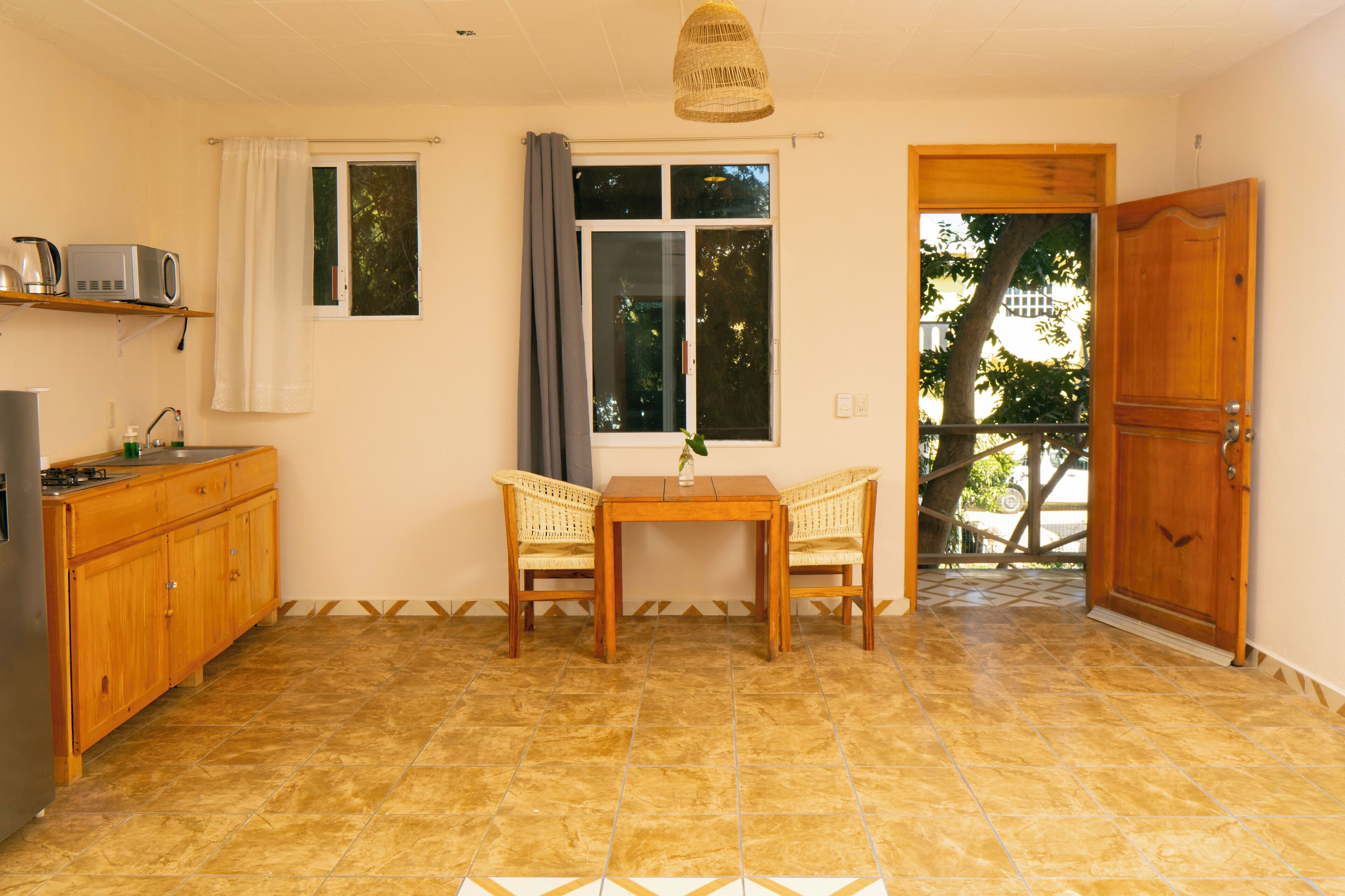 A kitchen with a dining area, a window with curtains, a door, and a tiled floor.