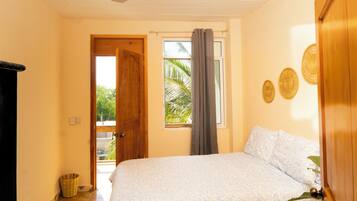 A bedroom with a bed, a window with curtains, a wooden door, and a wall with decorative plates.
