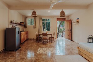 A compact kitchen with a refrigerator, stove, and wooden cabinets. There is a dining area with a table and chairs, and a view of the outdoors through a window.