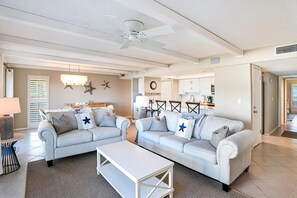 Ein großzügiges Wohnzimmer mit zwei hellgrauen Sofas, einem weißen Couchtisch und einem Deckenventilator.